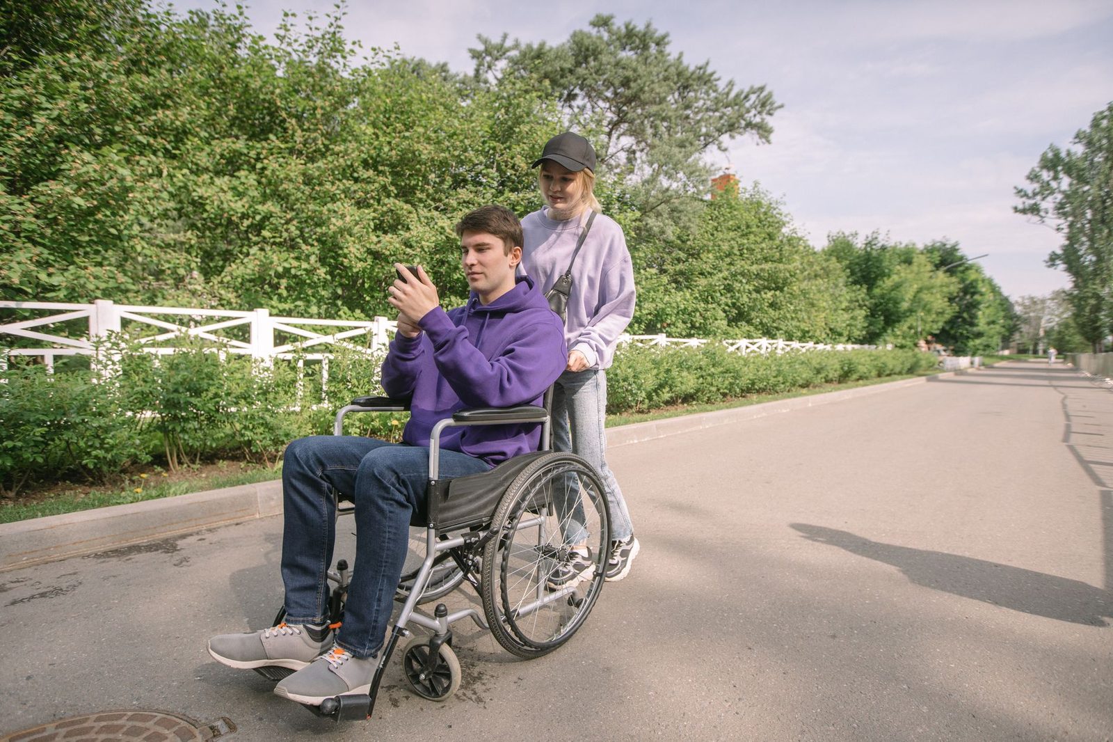 A smiling couple outdoors on a sunny day, with a man in a wheelchair laughing beside his partner.