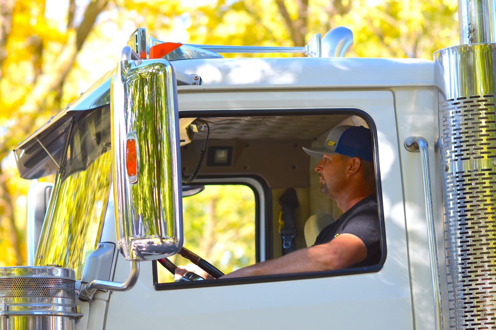 A truck driver at the wheel of a large commercial truck on a sunny highway.