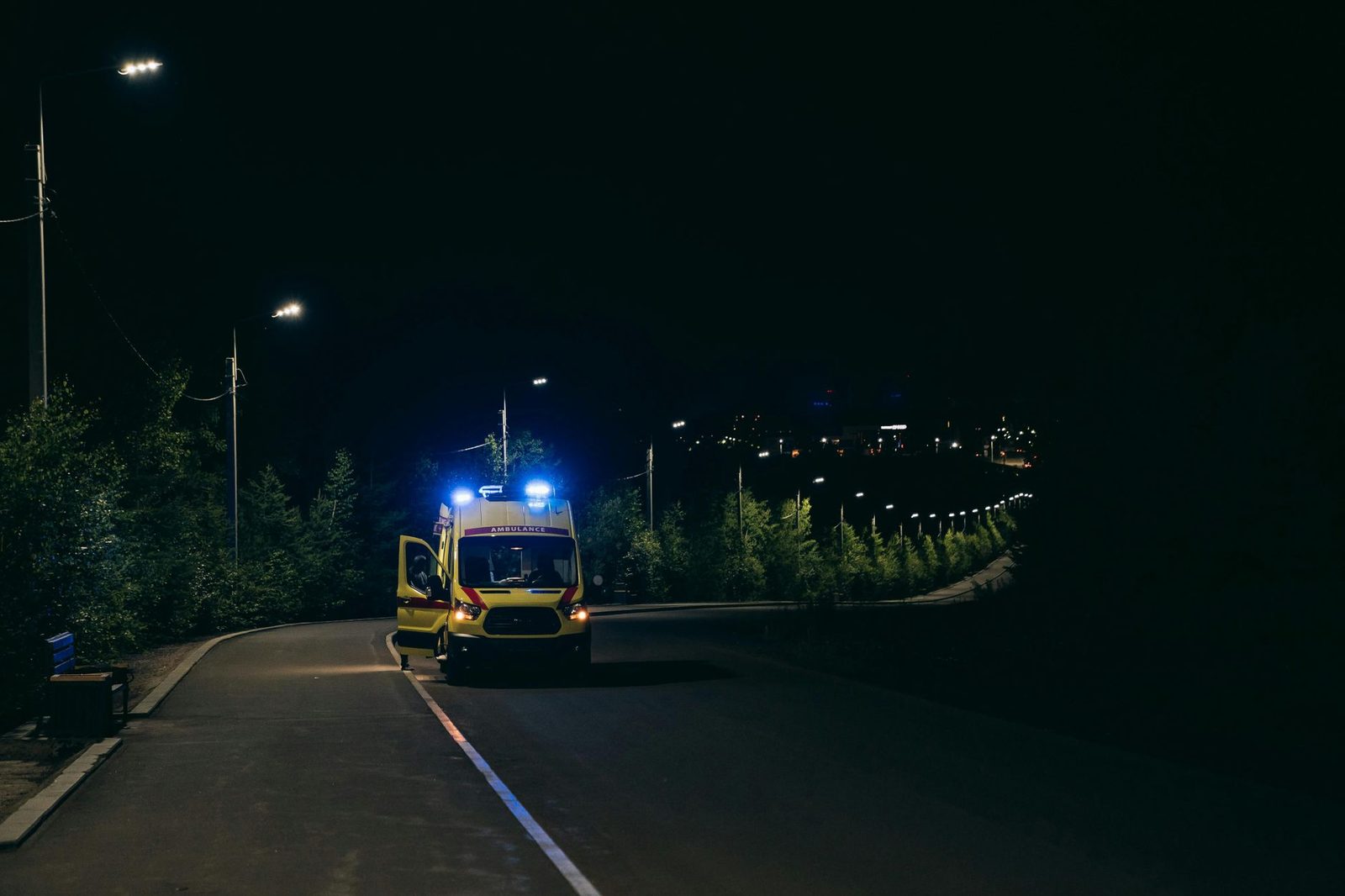Ambulance with flashing lights responding to emergency on rural road at night.