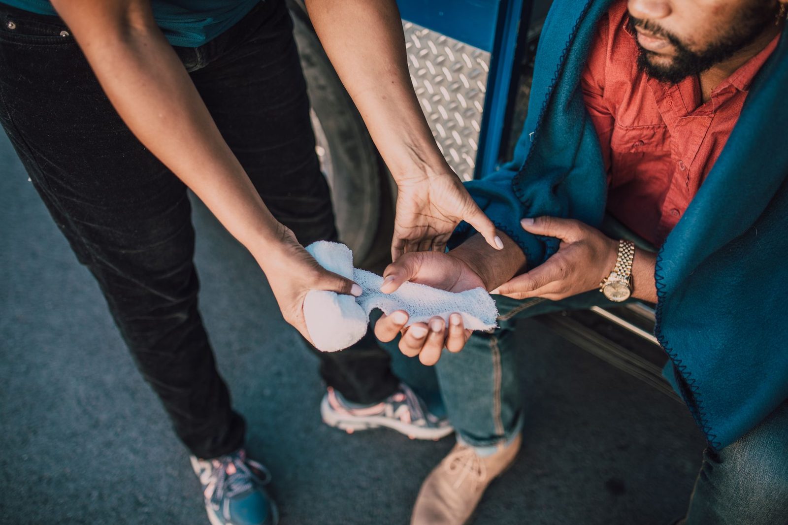 Close-up of a person pressing gauze onto an injured hand as part of first aid care.