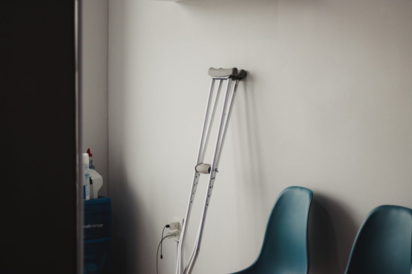Crutches leaning against wall beside blue chairs in waiting room.