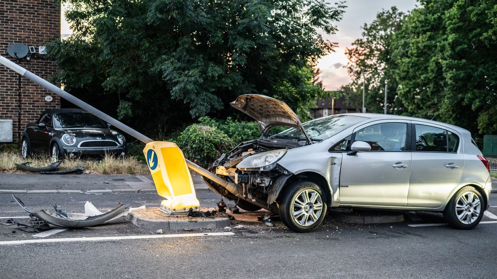 Damaged car crashed into lamp post on street at dusk.