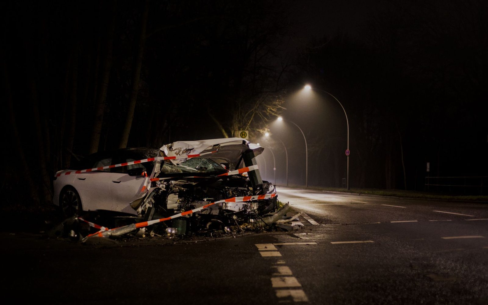 Damaged car wreckage on a dark street at night.