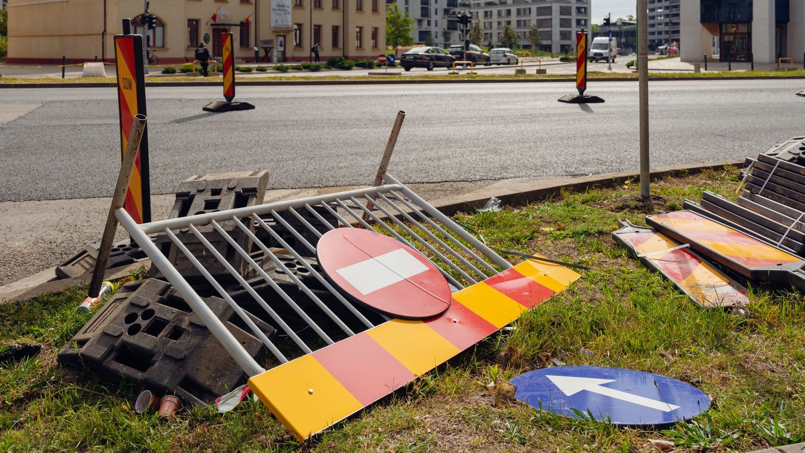 Discarded traffic signs and barriers lie beside a city road construction site.