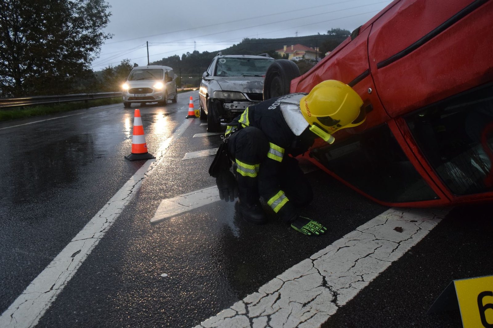 Firefighter assisting at overturned vehicle on wet road.