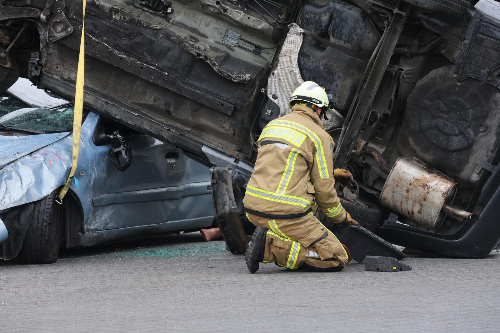 Firefighter in protective gear works at an overturned car after a crash, securing the scene during rescue.