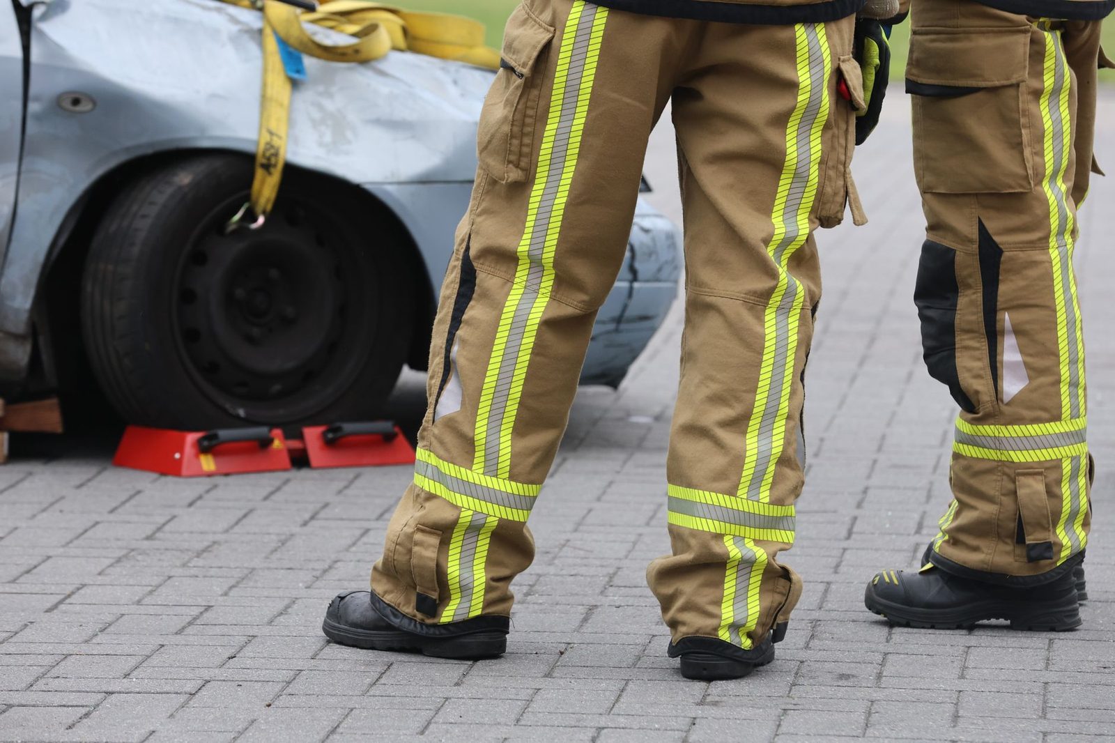 Firefighters in protective gear examining a damaged vehicle at accident scene.
