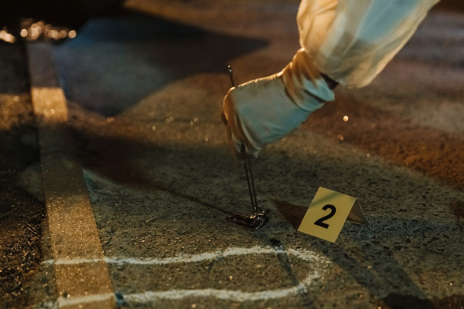 Gloved hands collect evidence from the ground at a nighttime crime scene.