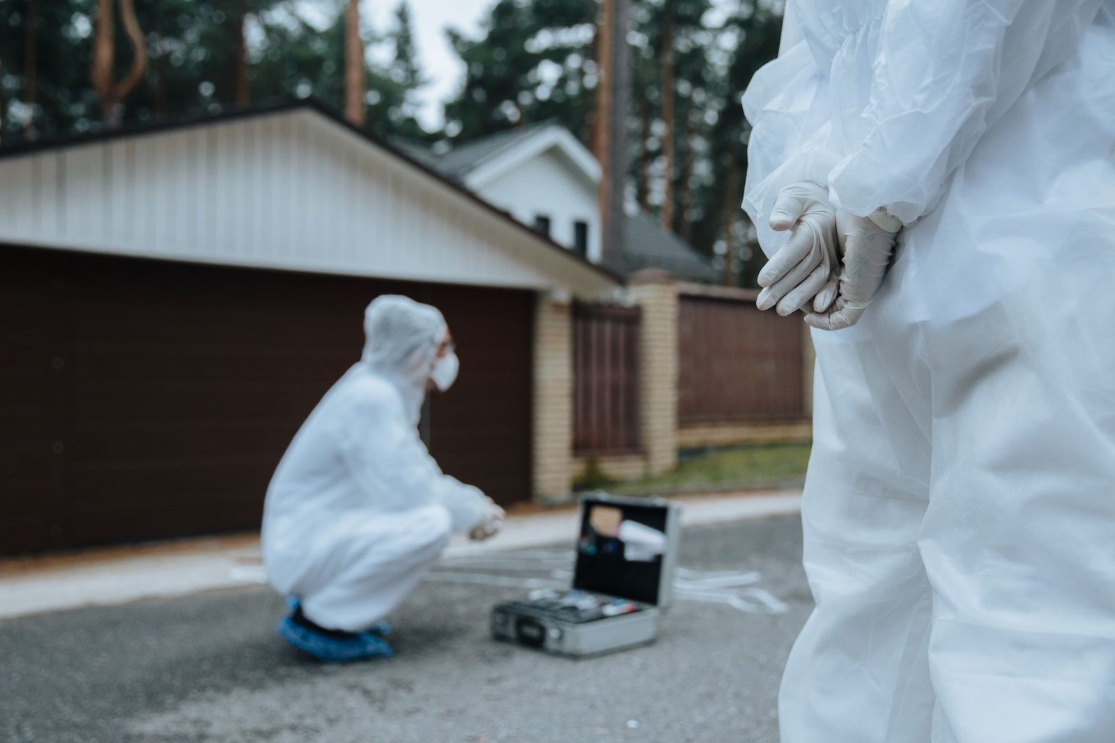 Investigators in white suits and masks examine a crime scene near a residential street.