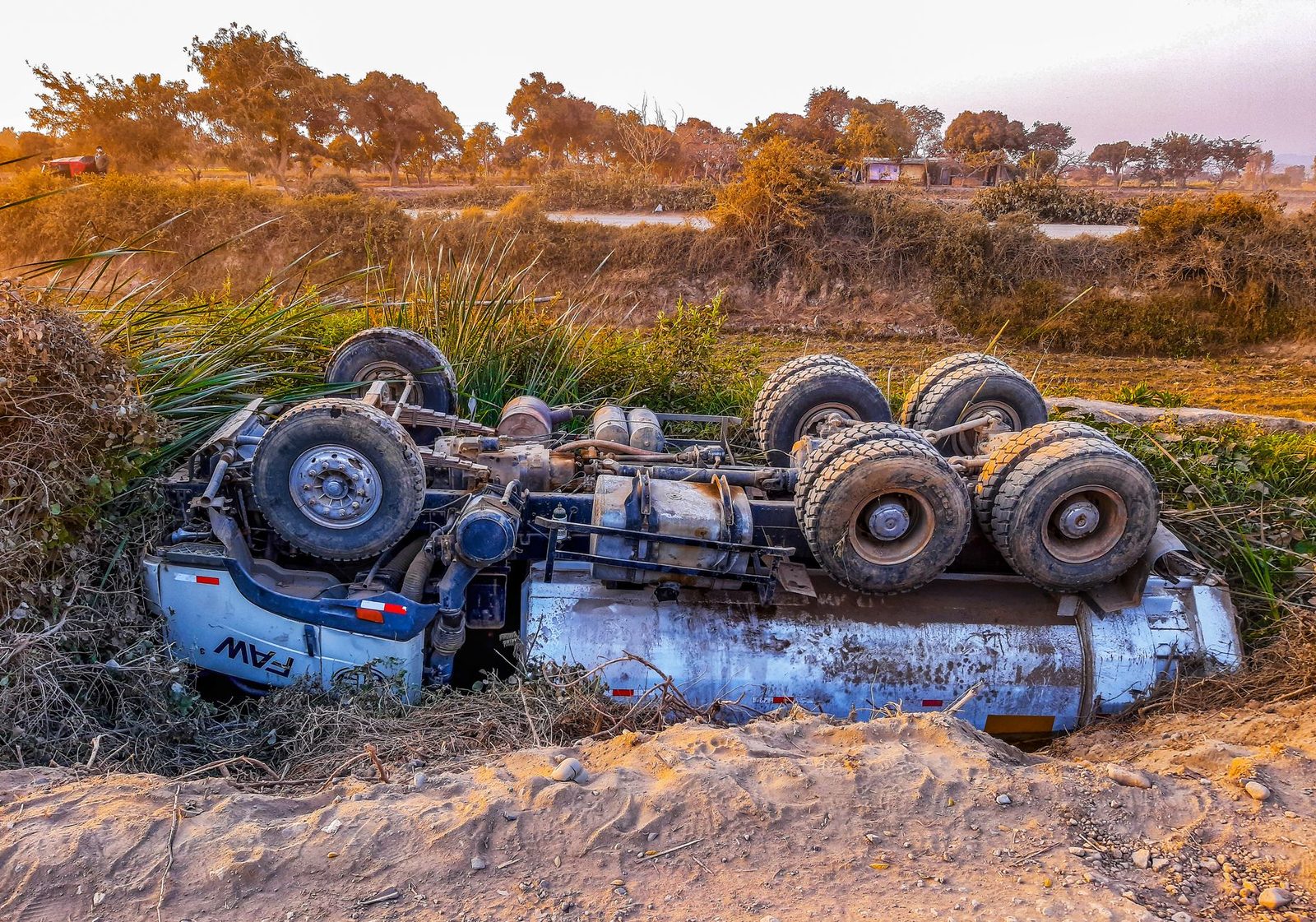 Overturned truck on a rural dirt road during daytime.