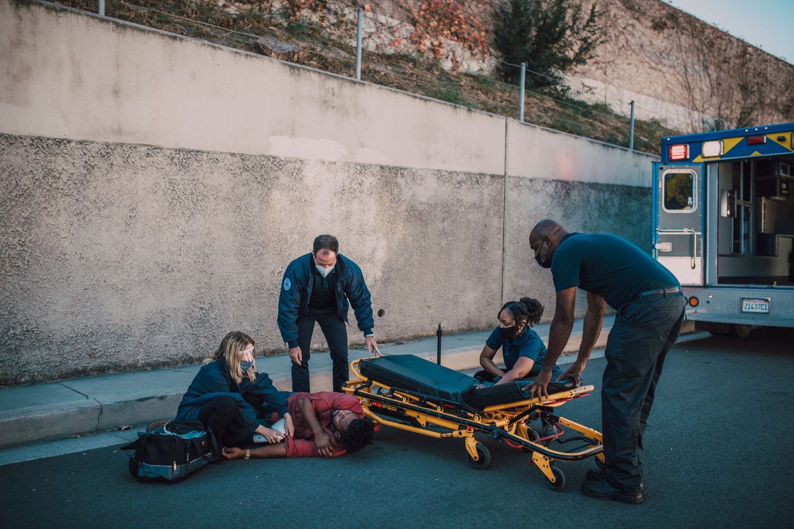 Paramedics attend to an injured person on a city street, with a stretcher beside them.