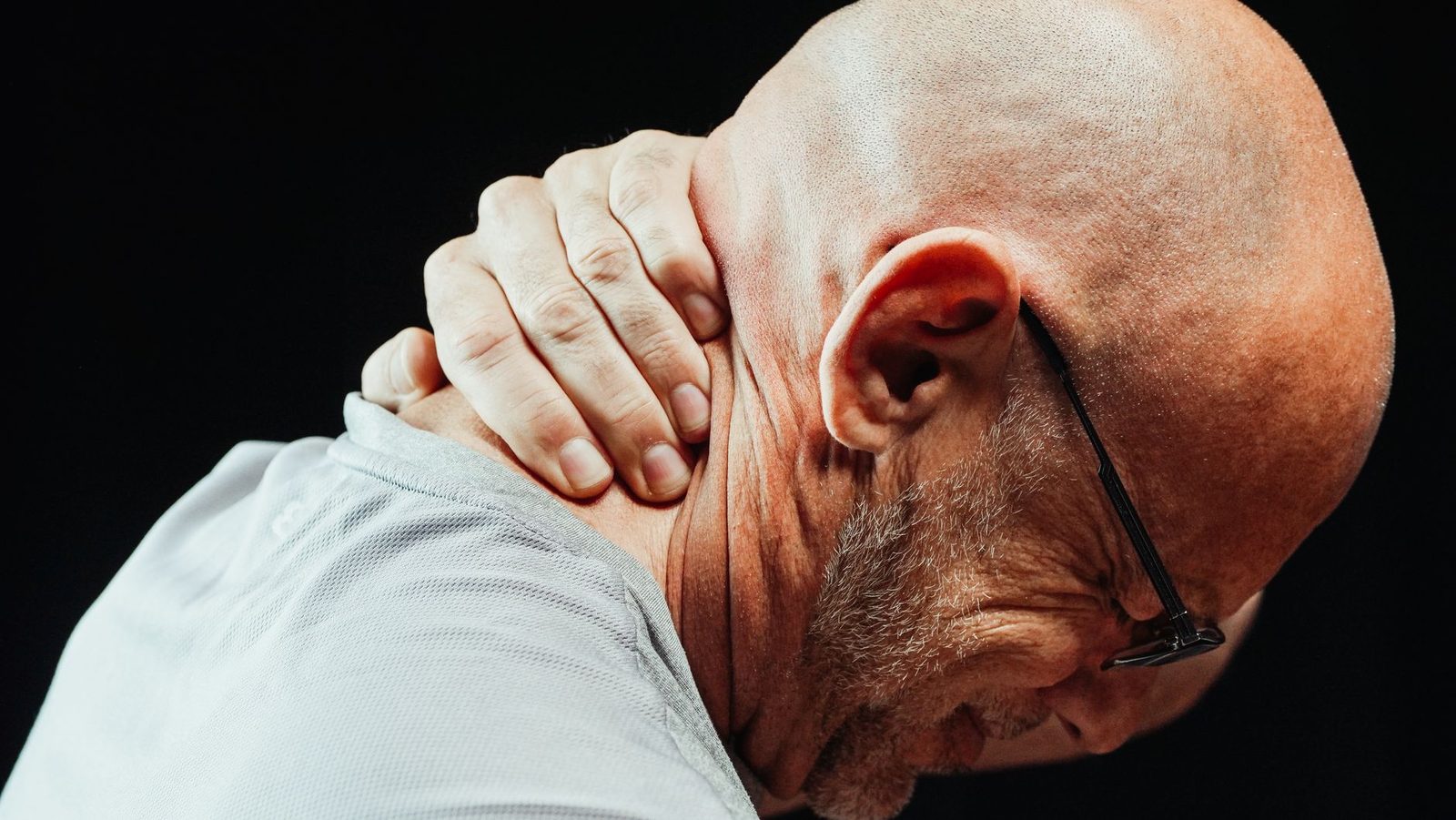 Side view of a senior man holding his neck, showing visible discomfort.