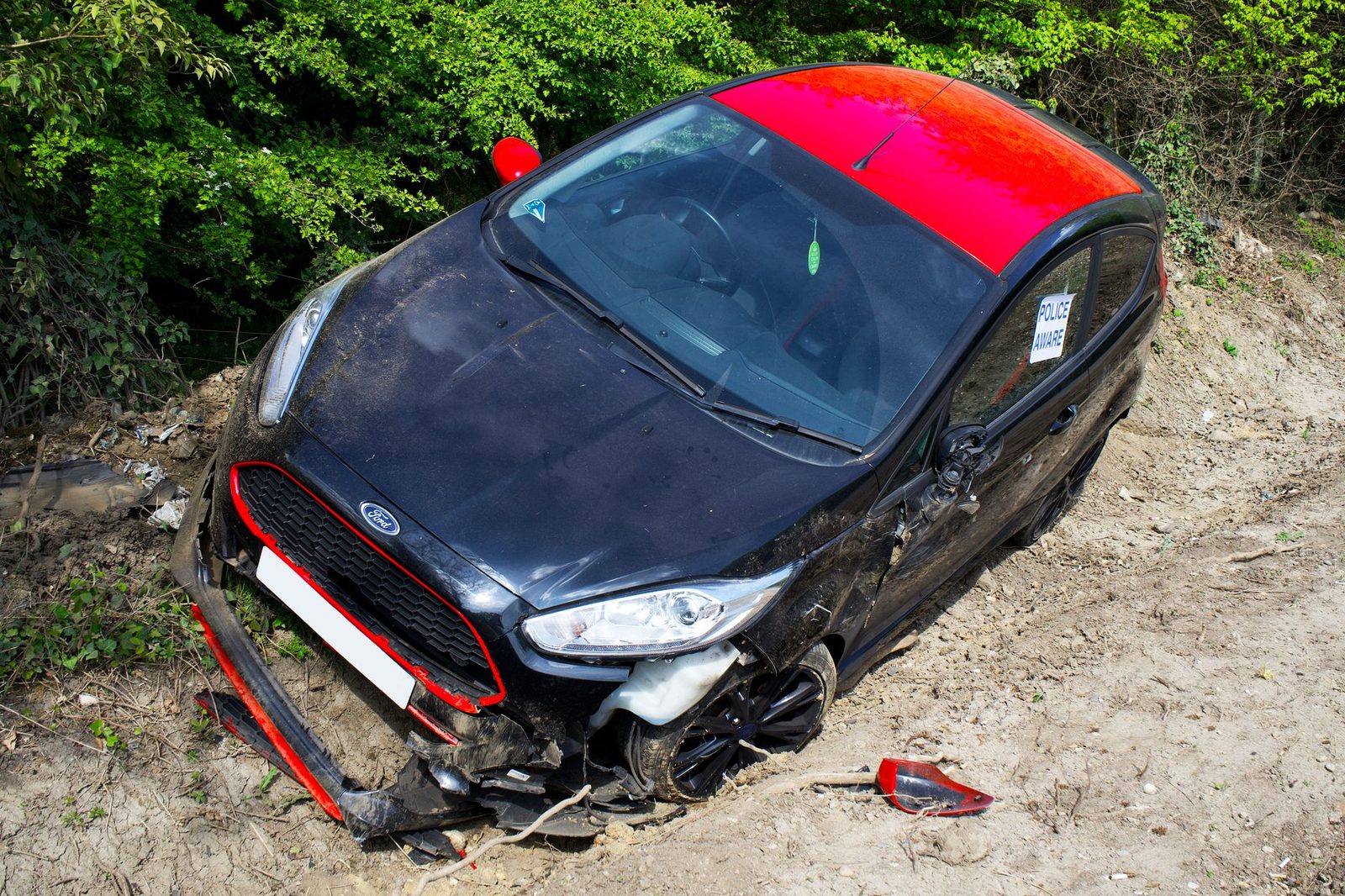 Severely damaged black and red Ford Fiesta abandoned off-road after collision.