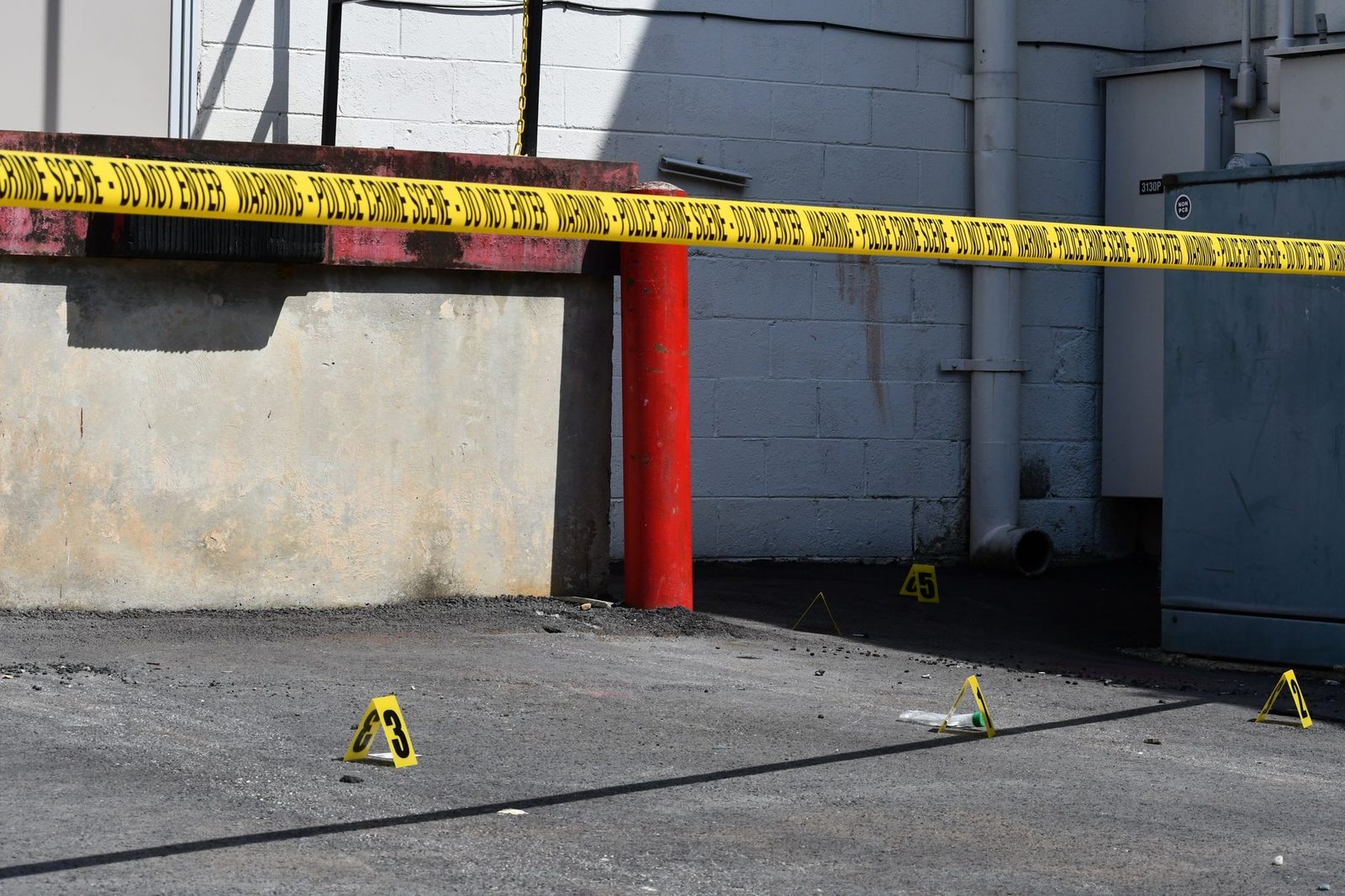 Sunlit city street with yellow caution tape and numbered evidence markers on the pavement.