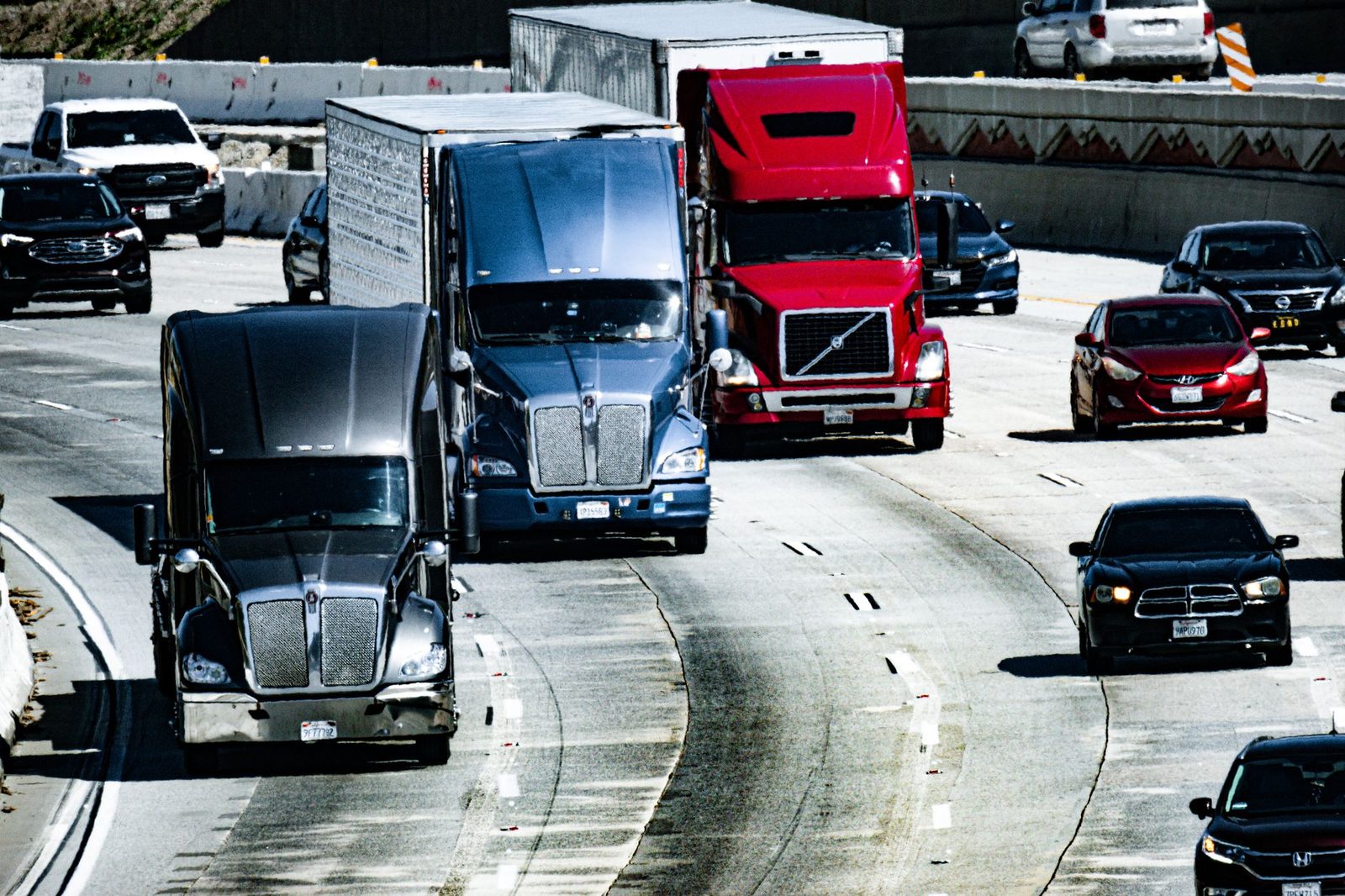 Trucks and cars travel along a congested city highway during the day.