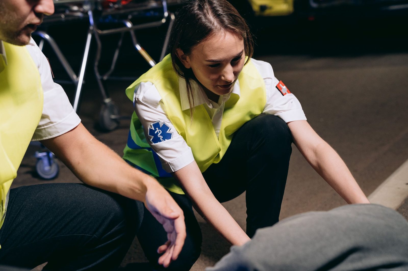 Two paramedics kneel beside a patient on the ground, providing emergency care.
