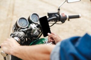 man holding handle bars and using mobile phone while sitting on a motorcycle at the beach