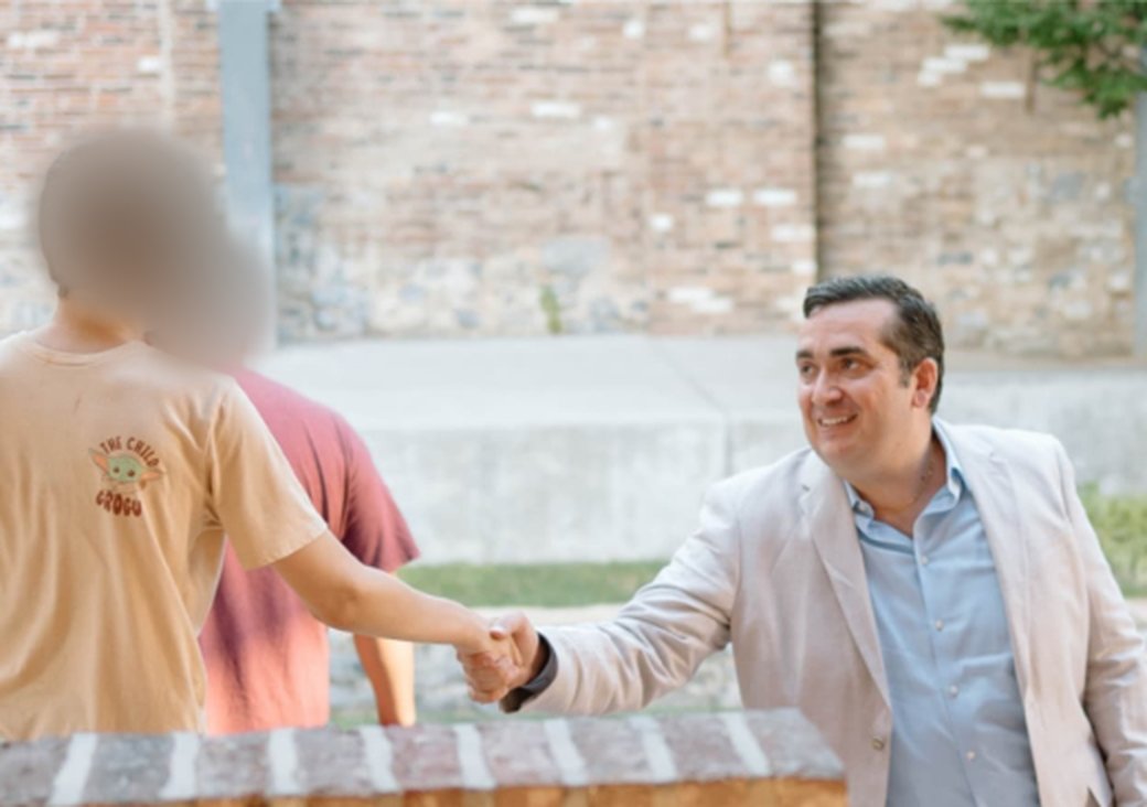 Beau Correll shaking hands with a student, seen from behind, at the firm's backpack giveaway