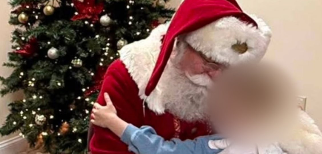 A child, face blurred for privacy, hugging Santa in front of a Christmas tree